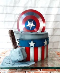 a captain america themed cake on a glass table with brick wall in the back ground