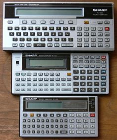 three calculators sitting side by side on top of a wooden table next to each other