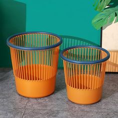 two orange and blue planters sitting next to each other on a cement floor in front of a green wall