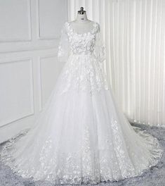 a white wedding dress with long sleeves and flowers on the skirt is displayed in front of a