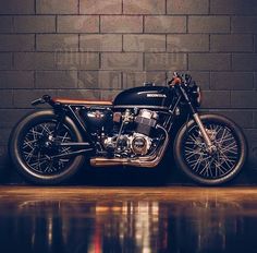 a black motorcycle parked in front of a brick wall with water reflecting on the ground