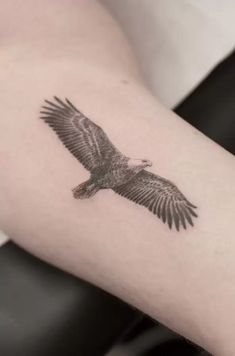 an eagle tattoo on the arm is shown in black and grey ink, with its wings spread