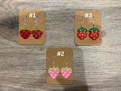 three small earrings with different designs on them sitting on top of a piece of cardboard