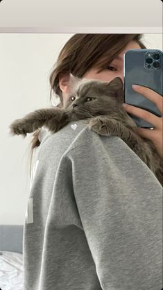 a woman taking a selfie with her cat on her shoulder while she is holding a cell phone