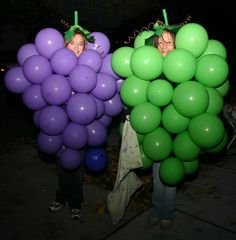 two people standing next to each other with balloons in the shape of grapes on their heads