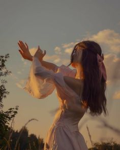 a woman in a white dress standing on top of a grass covered field with her arms outstretched