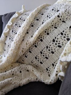 a white crocheted blanket sitting on top of a black couch next to a pillow