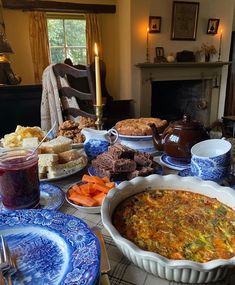 a table filled with plates and bowls of food next to a fireplace in a living room