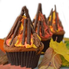 three cupcakes with chocolate frosting and candy sticks on them sitting next to leaves