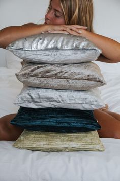 a woman is sitting on the bed with pillows stacked on top of her head and covering her face