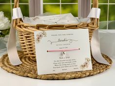 a basket with some cards inside of it on a table next to flowers and windows