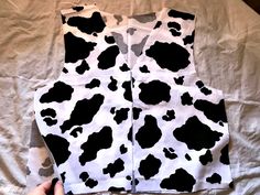 a person is holding up a cow print vest on top of a white sheet with black spots