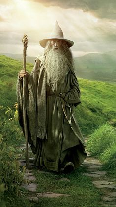 an old man with a long white beard holding a staff and walking on a path