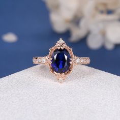 an oval shaped blue sapphire and diamond ring on display with white flowers in the background