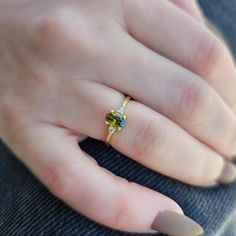 a woman's hand wearing a gold ring with green and blue stones on it