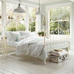 a white bed sitting in a bedroom next to two windows with lots of light on them