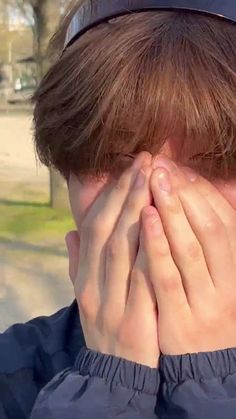 a boy covering his face with his hands while standing in front of a park bench