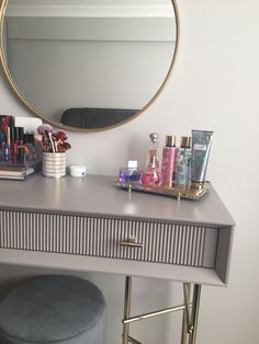 a vanity with a mirror, stool and various makeup products on the top shelf in front of it