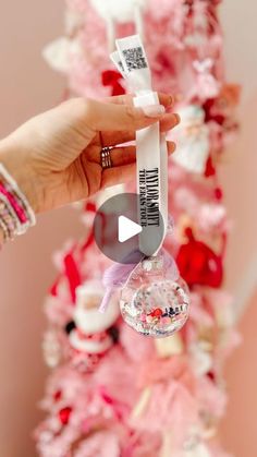 a person holding up a christmas ornament in front of a pink tree