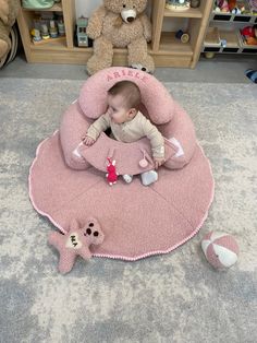 a baby sitting in a pink bean bag on the floor next to two teddy bears