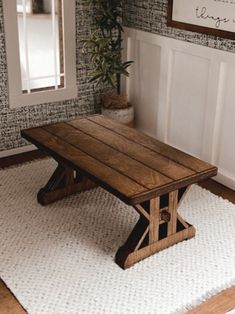 a wooden table sitting on top of a white rug next to a potted plant