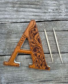 a wooden letter sitting on top of a table next to knitting needles