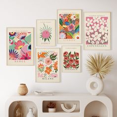 a white shelf topped with posters and vases next to a wall filled with flowers