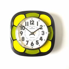 a black and yellow clock with numbers on the face is against a white wall background