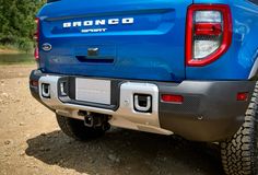 the rear end of a blue truck parked on top of a dirt field with trees in the background