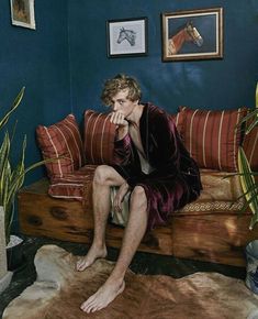 a man sitting on top of a couch in a living room next to a potted plant