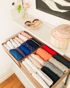 an open drawer filled with folded clothes on top of a wooden floor next to a painting