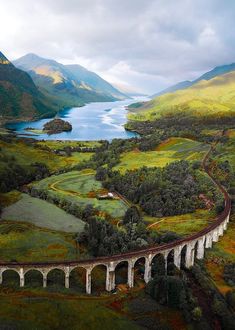 an aerial view of a train traveling over a bridge in the middle of green hills