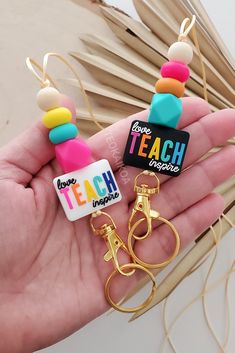 a person is holding two small keychains with colorful beads on them and the words teach inside