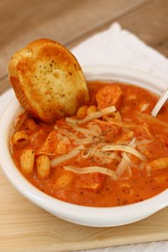 a white bowl filled with soup and bread on top of a wooden cutting board next to a napkin