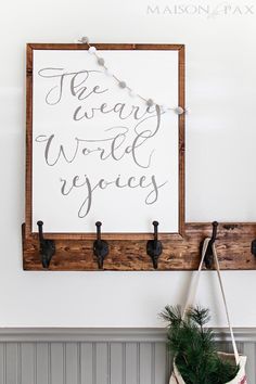 a wooden sign hanging on the wall next to a potted plant and coat rack