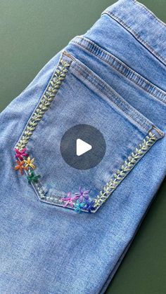 a pair of blue jeans with embroidered flowers on the side and a video play button