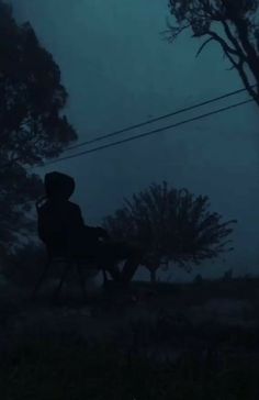 a person sitting in a chair under a tree on a foggy night with an umbrella over their head