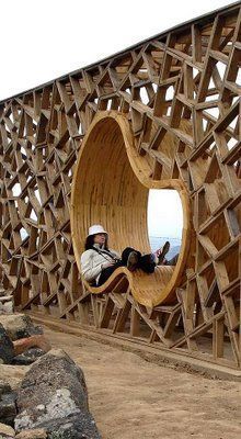 a man sitting in a wooden chair on top of a hill next to a large mirror