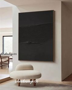 a living room with a white chair and a black painting on the wall above it