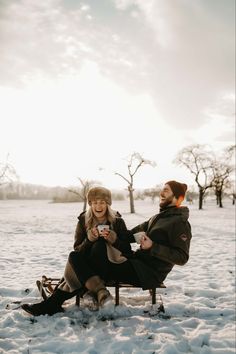 a man and woman sitting on a bench in the snow, laughing at each other