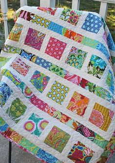 a colorful quilt sitting on top of a wooden chair next to a white fence and grass