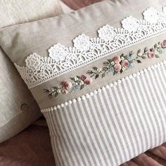 two pillows on a bed with white lace trimmings and pink flowers in between them