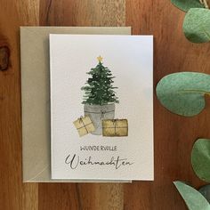 a card with a christmas tree and presents on it next to some green plant leaves