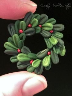 a hand holding a ring made out of green leaves and red berries on black background