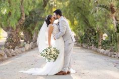 a bride and groom kissing in the middle of a dirt road surrounded by palm trees