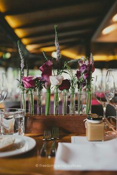 flowers in vases on a table with wine glasses and silverware next to it