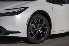 the front end of a white car with chrome spokes and black rims, parked in a parking lot