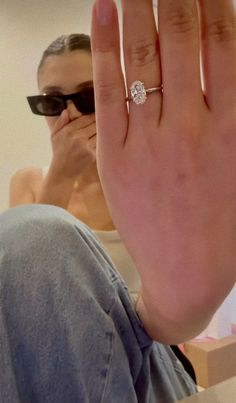 a woman wearing sunglasses is holding her hand up in front of her face with the ring on it