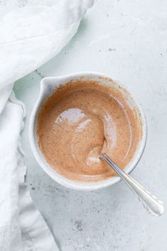 a white bowl filled with brown liquid on top of a white table cloth next to a spoon