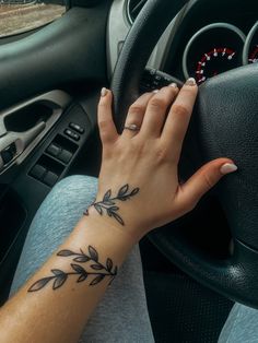 a woman's hand on the steering wheel of a car with an olive branch tattoo